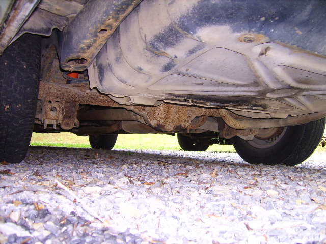 Underside of a rusty vintage car showing exhaust, suspension, and fuel tank.