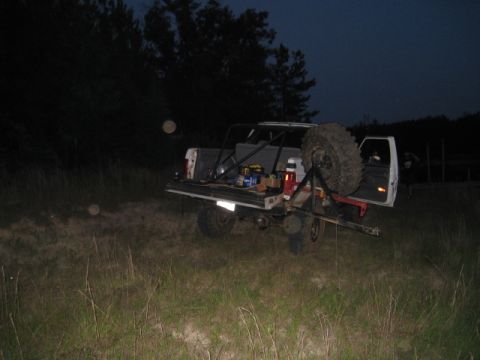 1996 Ford Bronco - Dusk shot of a white full-size SUV in a grassy field with the rear tailgate area open, a spare mud-terrain tire on a swing-out carrier and…