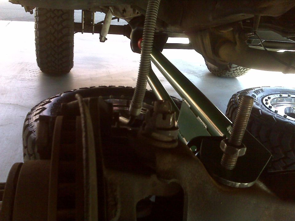 Close-up of off-road vehicle suspension with large tire, brake rotor, and green suspension arms.