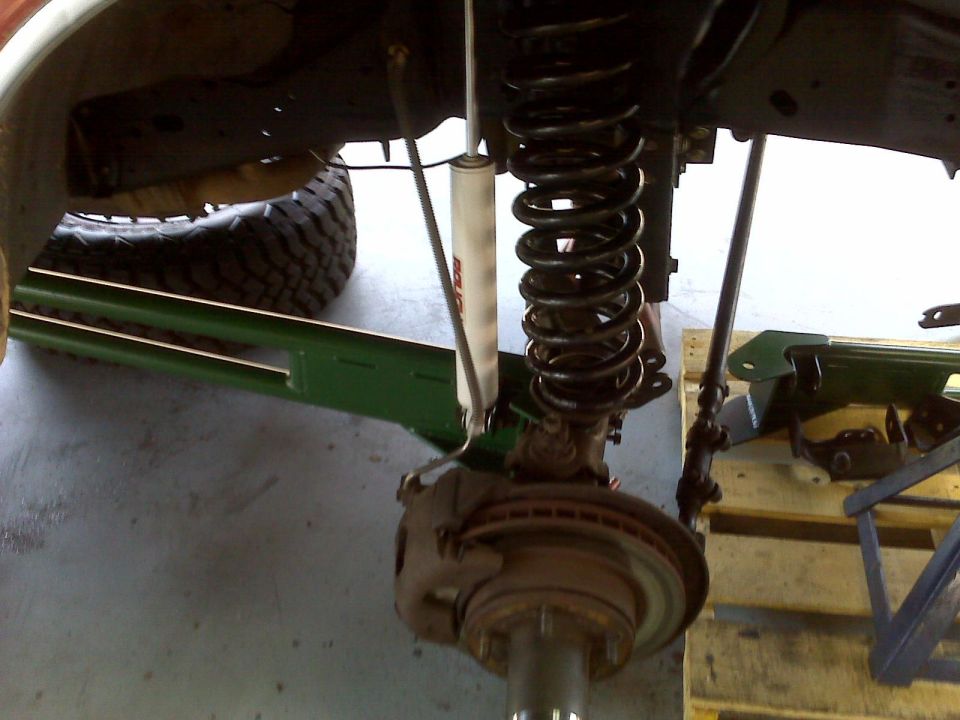 Underside of a vehicle showing suspension, coil spring, shock, and brake assembly.