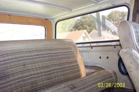 1979 Ford Bronco — Interior shot of a vehicle, showing striped seats and door paneling. Houses visible through the window