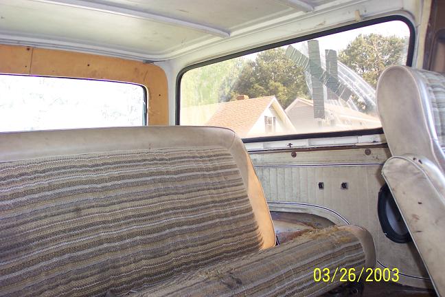 Interior shot of a vehicle, showing striped seats and door paneling. Houses visible through the window