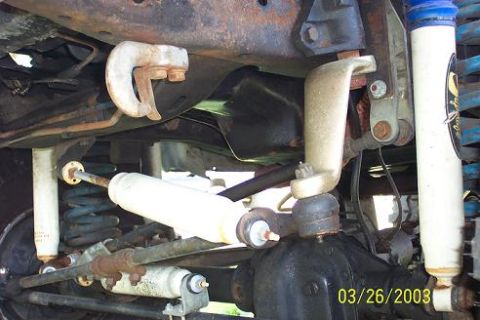 1979 Ford Bronco — Undercarriage of a vehicle with visible suspension components, shocks, and differential. Rusty metal parts ar…