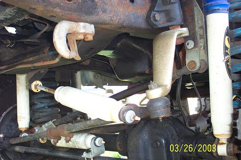 Undercarriage of a vehicle with visible suspension components, shocks, and differential. Rusty metal parts are prominent