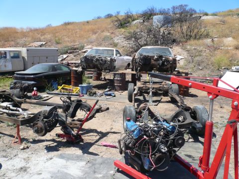1975 Ford Ranchero - Disassembled car parts and engines are scattered across a junkyard lot under a clear sky.