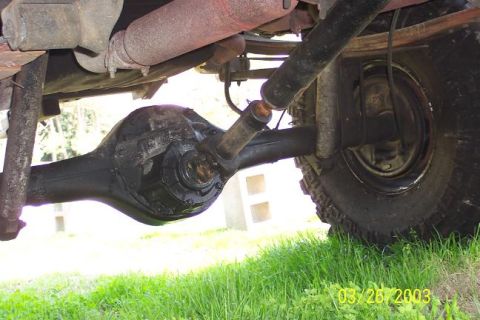 1979 Ford Bronco — Underside view of a vehicle's rear axle, differential, driveshaft, and tire, with grass in the foreground
