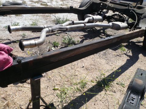 1975 Ford Ranchero - The frame of a vehicle, showing its exhaust system, is supported by stands on the ground.
