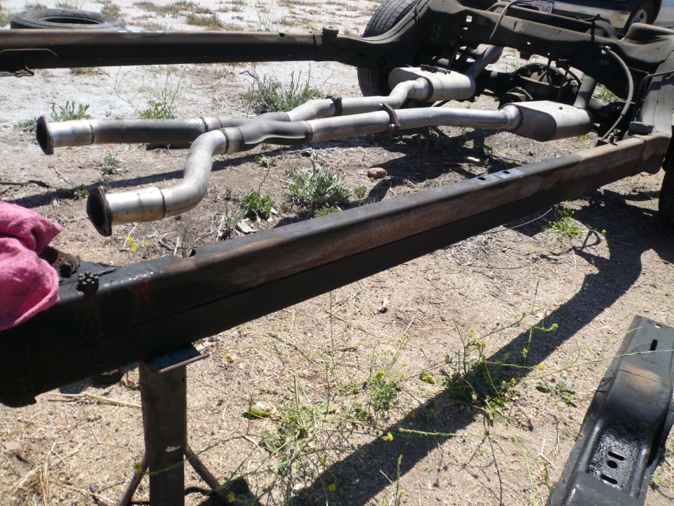 vehicle frame with dual exhaust pipes and mufflers, resting on stands