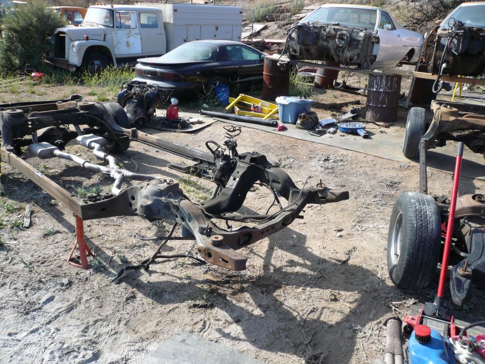 Car chassis on red jack stands, with other vehicle parts and frames scattered in a junkyard