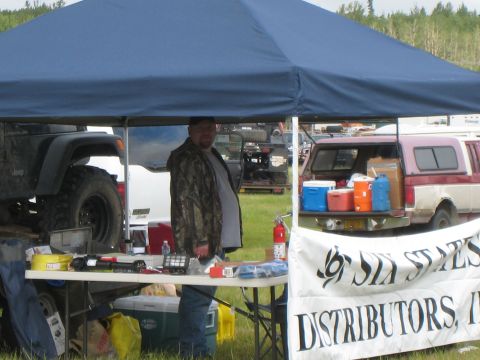 2000 Ford E350 - A man stands under a tent at an outdoor event with a Jeep and a pickup truck visible.