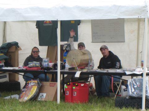 2000 Ford E350 - Three people are seated at a table under a white tent, with various items displayed, including raffle prizes and a whiteboard with writing.