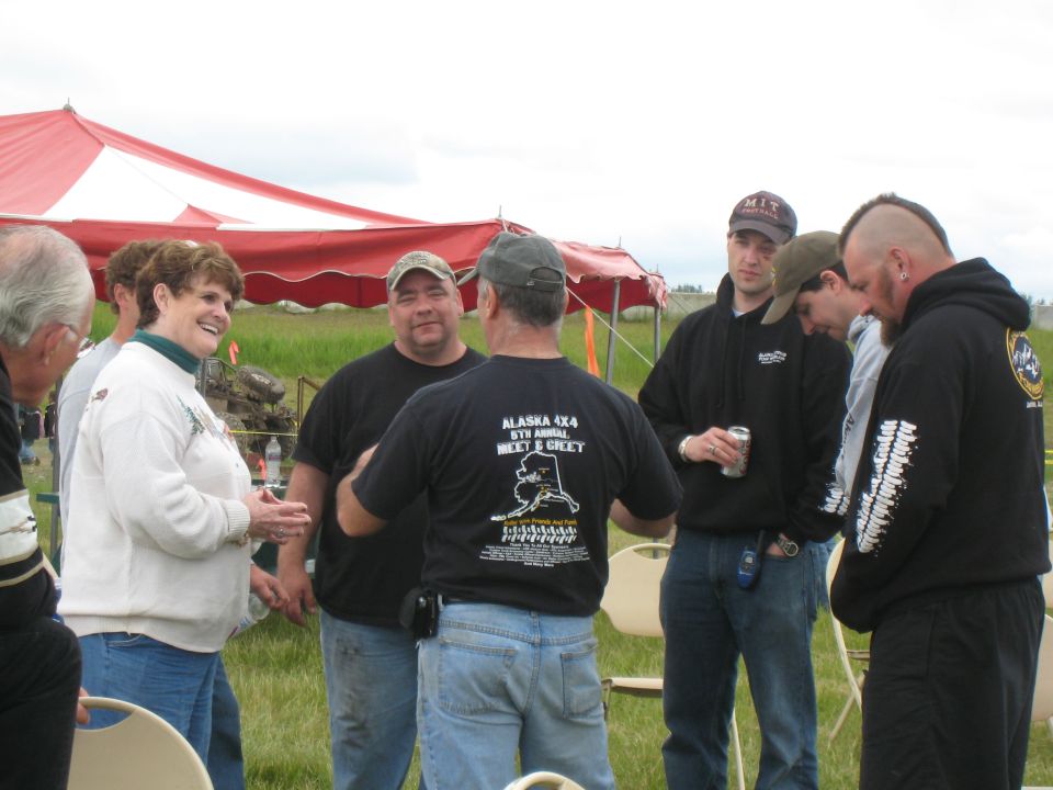 People gathered under a red and white tent, some talking, one holding a can