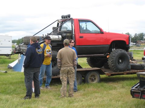 2000 Ford E350 - A heavily modified red pickup truck with oversized tires is parked on a trailer, ready for transport or display.
