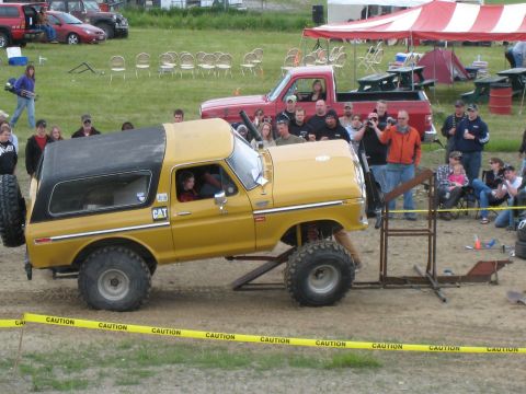 2000 Ford E350 - A modified yellow SUV with a camper shell is positioned on a ramp, with spectators gathered around.