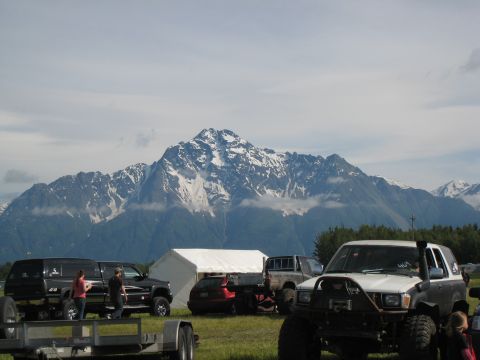 2000 Ford E350 - Several off-road vehicles are parked in a grassy field with a large, snow-capped mountain range in the background.