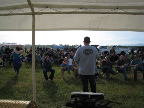 2000 Ford E350 - An outdoor event draws a crowd seated on the grass under a large tent, with several vehicles parked in the distance.