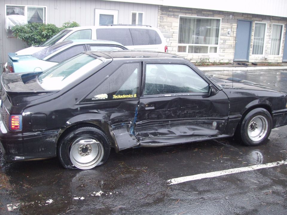 Black Ford hatchback with major side collision damage in a parking lot