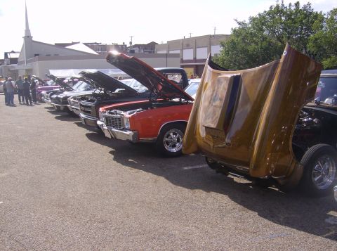 1970 Ford Ranchero - A line of vehicles are parked with their hoods open, displaying their engines at an outdoor event.
