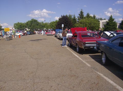 1970 Ford Ranchero - A red muscle car with its hood open is parked at a car show. Several other vehicles are visible in the background.