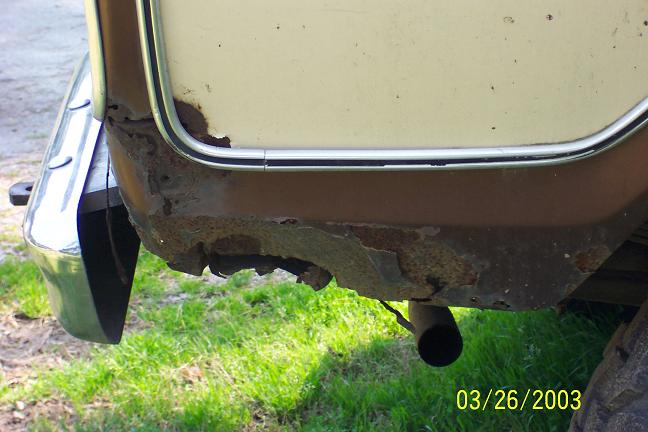 rusted rear quarter panel and bumper of a vehicle, with exhaust pipe visible