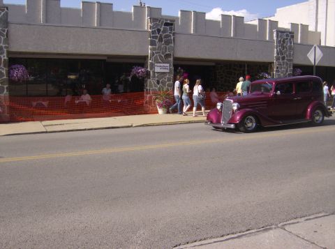 1970 Ford Ranchero - A maroon sedan drives down the street in front of a building with outdoor seating.