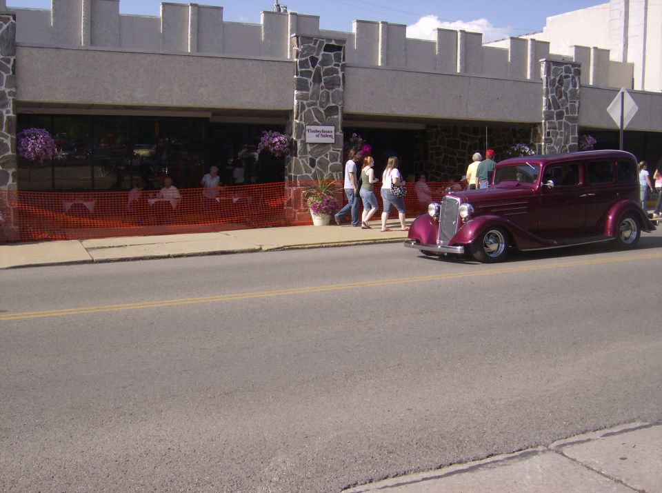 Maroon sedan driving past a building with people outside