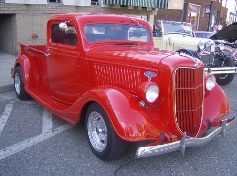 1970 Ford Ranchero - A bright red 1935 Ford pickup truck is displayed outdoors with other classic vehicles.