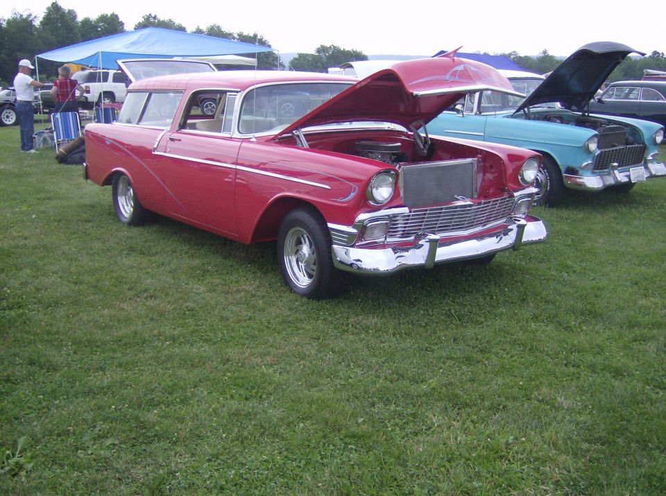 Red 1950s station wagon with hood open, parked on grass next to a blue car.