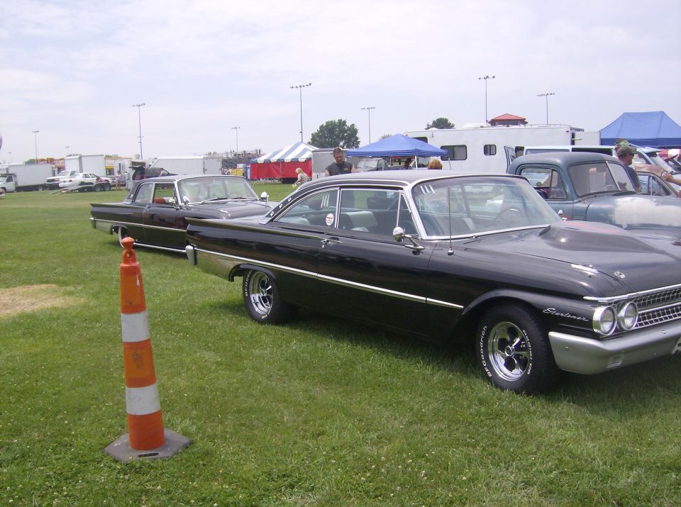 Black 1960 Ford Starliner two-door hardtop with chrome trim and custom wheels parked on grass.