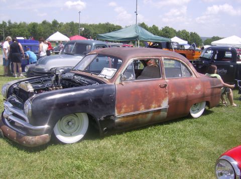 1970 Ford Ranchero - Customized sedan with a rusty patina and lowered stance sits on display at a car show.