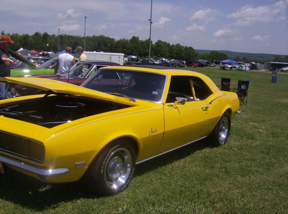 Yellow 1967 Chevrolet Camaro coupe with hood open, parked on grass at an outdoor event