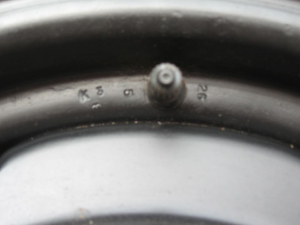 Close-up of a tire valve stem and numbers stamped on a car wheel rim.