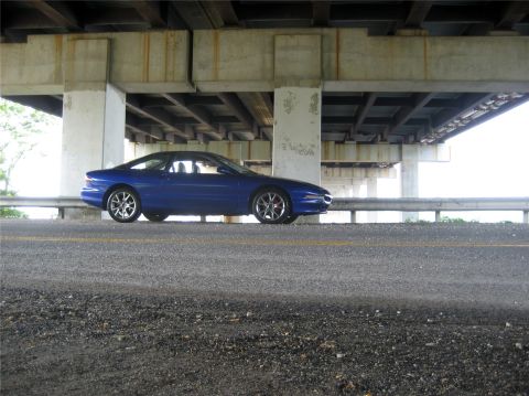 1993 Ford Probe - A blue 1993 Ford Probe is parked under a concrete overpass. The car is viewed from the side, with the front of the vehicle on the right.