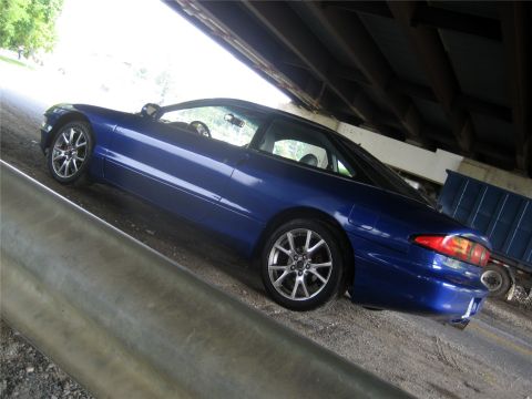 1993 Ford Probe - A blue 1993 Ford Probe is parked under a bridge, showing its side profile and rear quarter panel. The car has aftermarket silver rims and a…