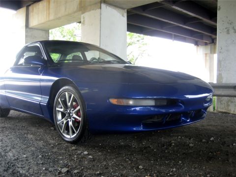 1993 Ford Probe - A blue 1993 Ford Probe is parked on a gravel surface under an overpass. The front passenger side of the car is prominently featured, showin…