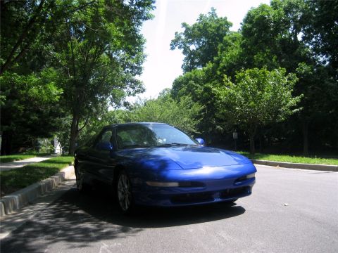 1993 Ford Probe - A shiny blue 1993 Ford Probe is parked on the side of a residential street, casting shadows from overhead trees.