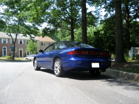 1993 Ford Probe - The rear passenger side of a blue 1993 Ford Probe is parked on a residential street with trees and townhouses in the background.