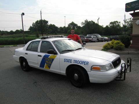 1991 Ford LTD Crown Victoria - man in a red shirt and sunglasses stands behind the open driver door of a white New Jersey State Police Ford Crown Victoria.