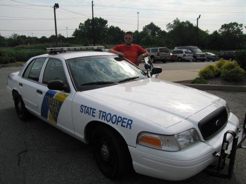1991 Ford LTD Crown Victoria - man in a red shirt stands at the open door of a white New Jersey State Police Ford Crown Victoria seen from the front three-quarter angle.