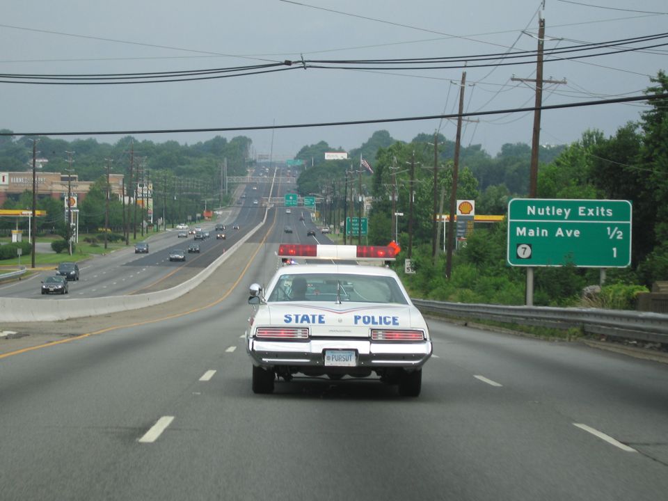 White State Police sedan driving on highway past Nutley exits sign