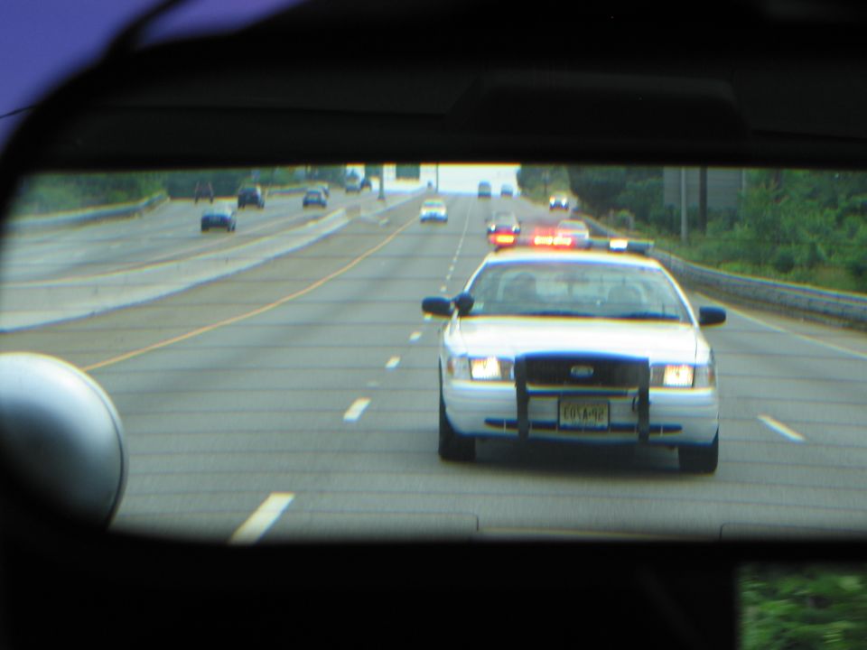 View through car window of white Crown Victoria police car following on highway