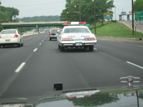 1991 Ford LTD Crown Victoria - white State Police sedan with roof light bar reading STATE POLICE drives ahead on a multi-lane highway near a parkway sign.