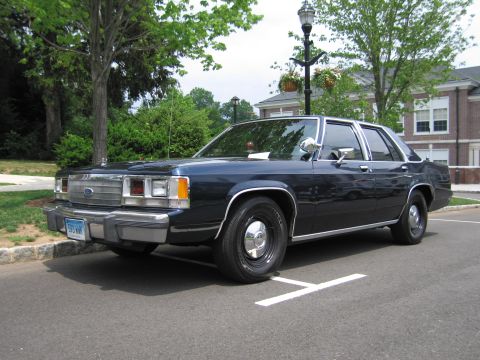 1991 Ford LTD Crown Victoria - dark blue Ford LTD Crown Victoria sedan parked at a curb near brick buildings, shown front three-quarter with a lamp post behind.