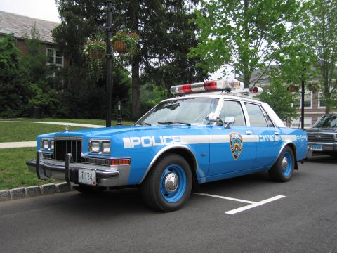 1991 Ford LTD Crown Victoria - Front three-quarter view of a blue-and-white NYPD Highway Patrol Dodge sedan with NYPD shield and roof light bar parked at a curb.