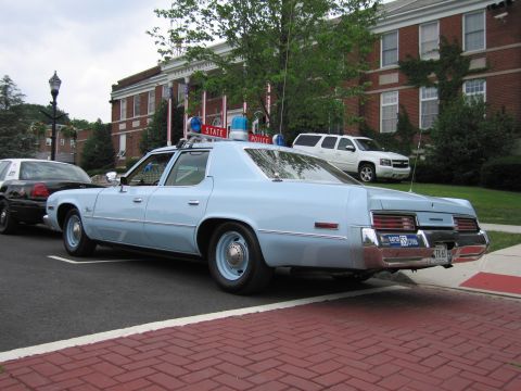 1991 Ford LTD Crown Victoria - light-blue full-size 1970s State Police sedan with a roof lightbar parked rear three-quarter on red brick pavement.