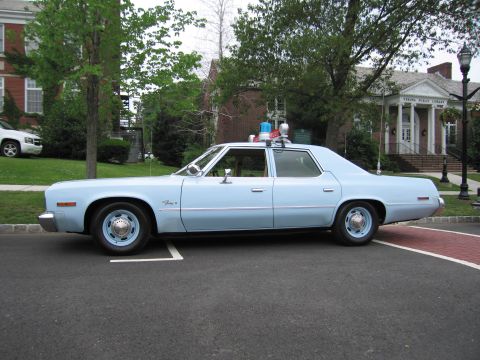 1991 Ford LTD Crown Victoria - Driver-side profile of a light-blue Plymouth Fury State Police sedan with roof beacons parked before a brick library.