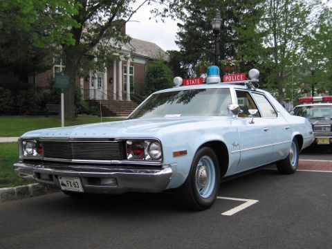 1991 Ford LTD Crown Victoria - Light-blue Plymouth Fury State Police sedan shown front three-quarter with a chrome grille and roof beacons, parked at a curb.