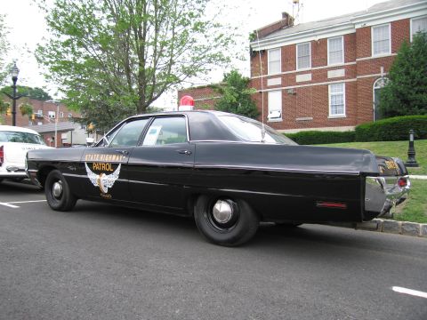 1991 Ford LTD Crown Victoria - black Ohio State Highway Patrol sedan bearing a gold winged emblem, parked rear three-quarter on a tree-lined street.