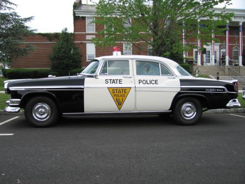1991 Ford LTD Crown Victoria - Driver-side profile of a 1950s black-and-white New Jersey State Police Chrysler sedan with a single red roof beacon.