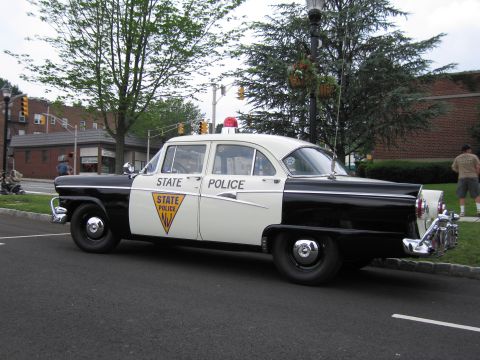 1991 Ford LTD Crown Victoria - Driver-side profile of a 1950s black-and-white New Jersey State Police Ford sedan with chrome trim and a rear continental kit.